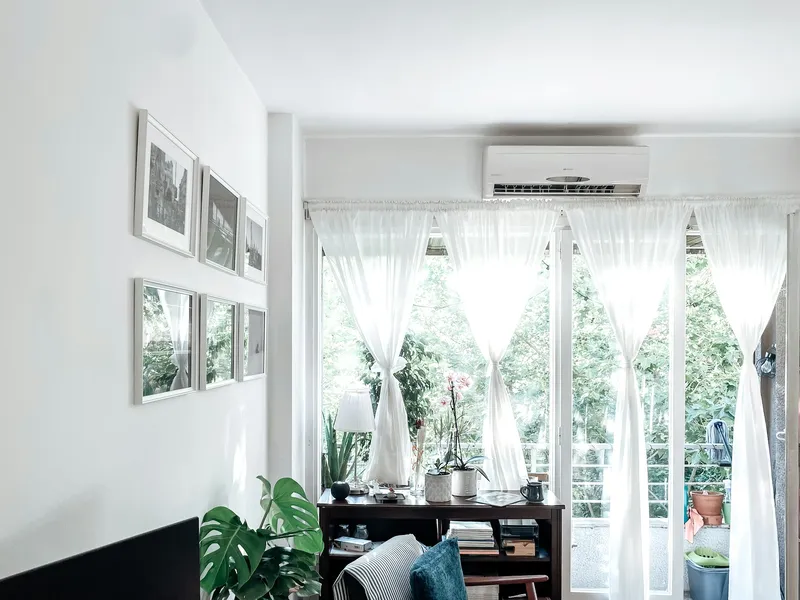 Sala luminosa com mesa e janela com cortinas, com uma unidade de ar condicionado de parede